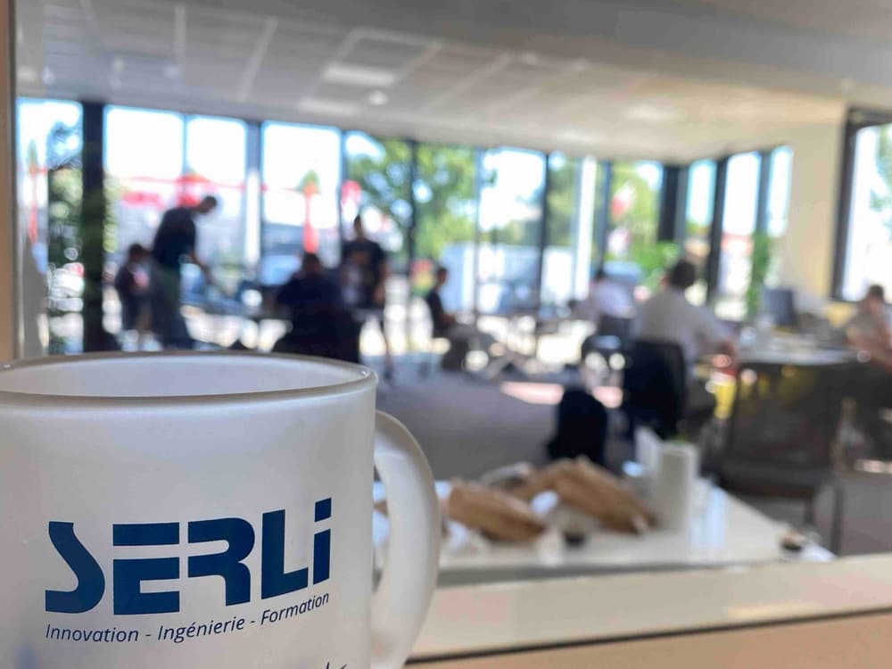 Une tasse Serli au premier plan, et des Serliens qui travaillent ensemble dans l'espace de travail